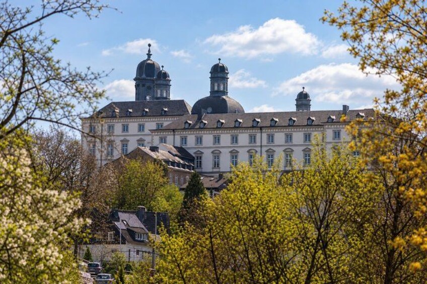 A large historic building with multiple domes and a symmetrical facade, surrounded by trees and other buildings. 5
