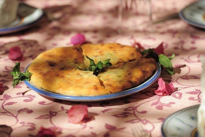 A round dish with a golden-brown crust, garnished with mint leaves, on a patterned tablecloth. 4
