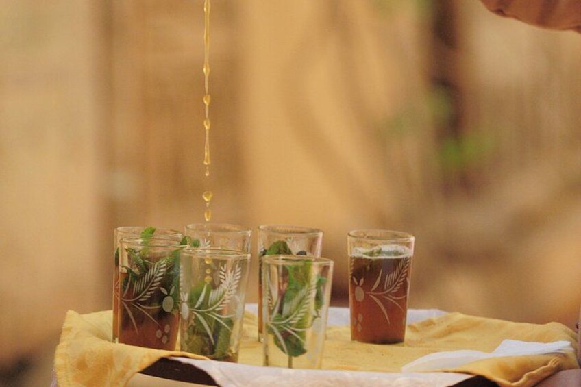 Four glasses with plant decorations, one with a dark liquid, and a hand pouring a yellow liquid into the first glass. 4