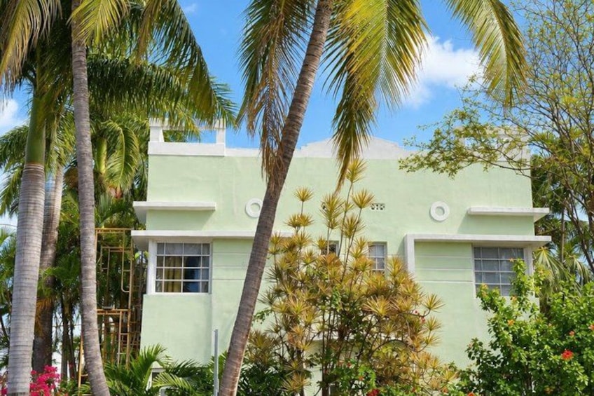 A light green building with a flat roof, surrounded by palm trees and tropical vegetation. 4