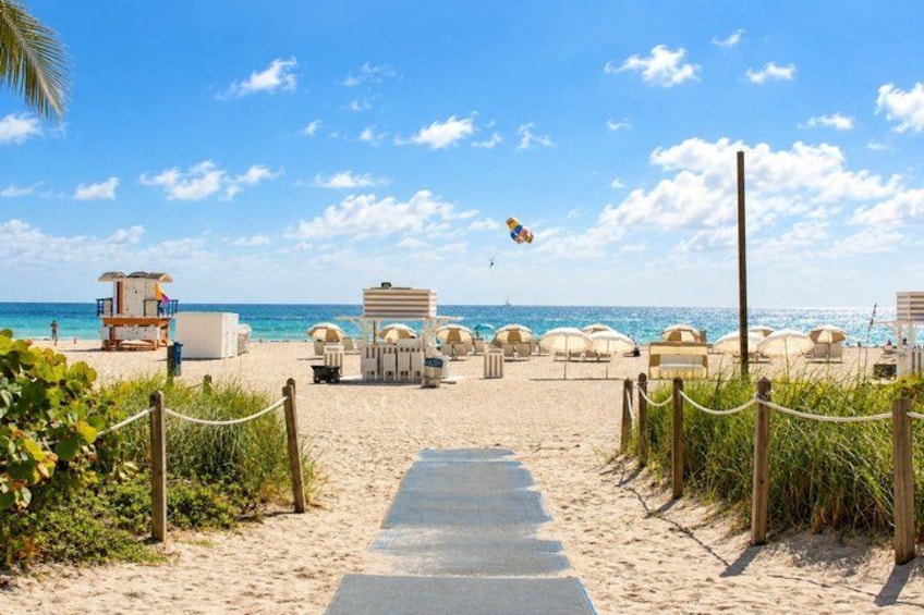 A beach with a paved walkway, beach umbrellas, and a lifeguard tower. 3