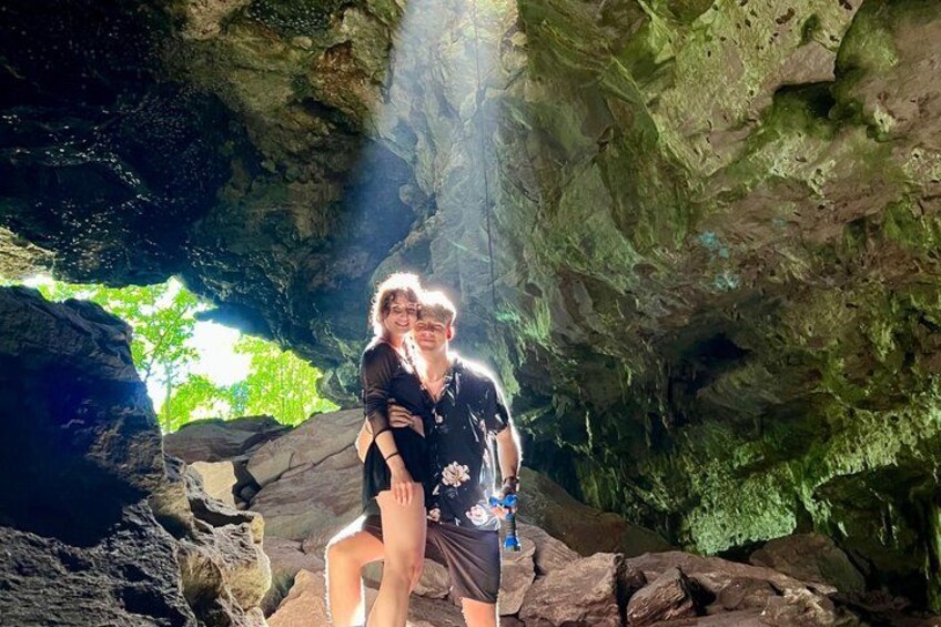 Two people standing in a cave with rocky walls and a natural light source. 2