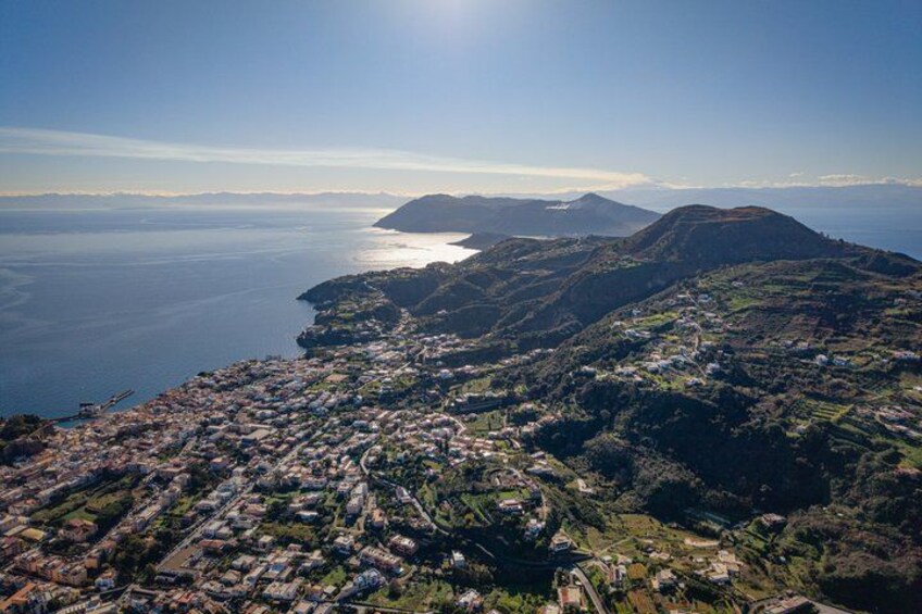 A coastal landscape with a town nestled in the valley, a body of water, and distant mountains. 4