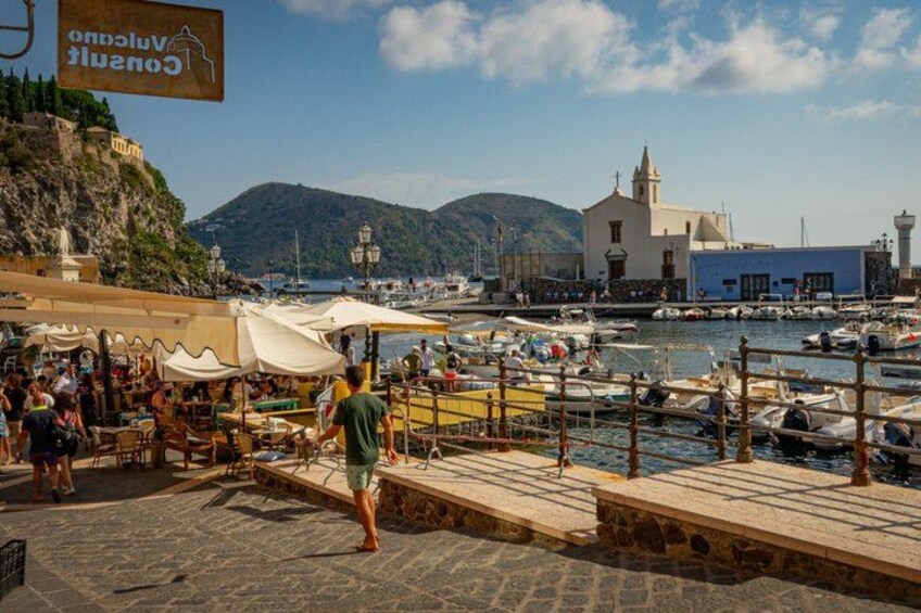A coastal town with a marina, people walking, and a church. 5