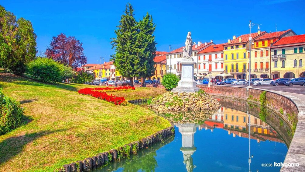 Ein Park mit einem Teich, einer Statue und farbenfrohen Gebäuden im Hintergrund. 1
