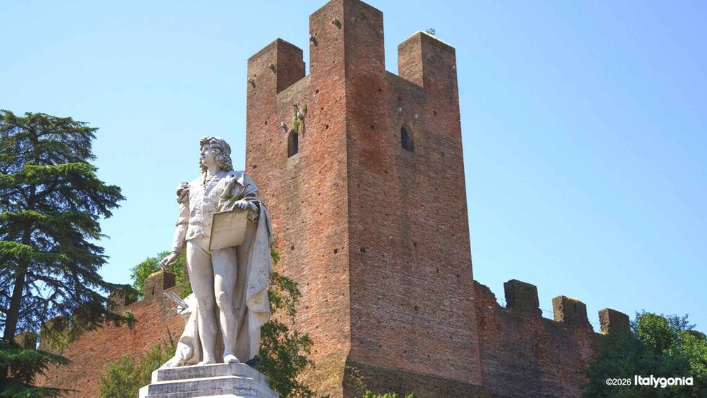 Eine Statue eines Manns, der ein Buch hält, ein Backsteinturm und Bäume im Hintergrund. 2