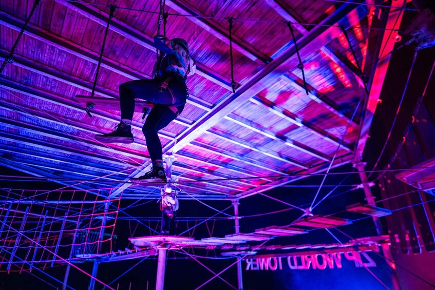 A person performing an aerial act on a trapeze with a net below, in a brightly lit indoor setting. 5