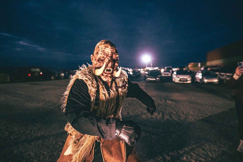 A person in a costume with a mask and horns, holding a prop, in a parking lot at night. 2