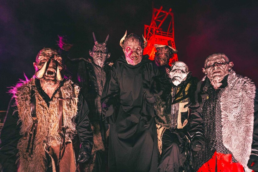 A group of people in costumes with a red structure in the background. 1