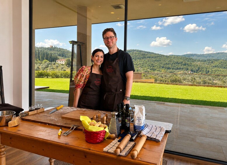 Un couple se tient dans une cuisine, avec une vue panoramique sur des collines verdoyantes et un bâtiment visible au loin. 1