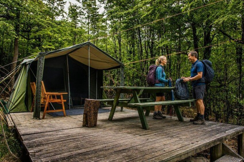 A tented camping area with a picnic table and a wooden deck. 3