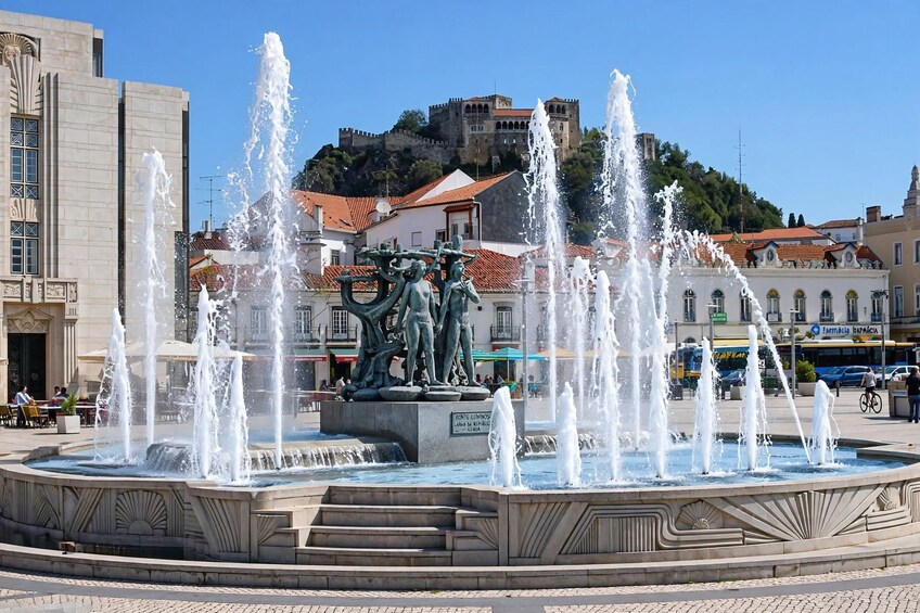 A public fountain with multiple water jets, a statue in the center, and a historic building in the background. 5