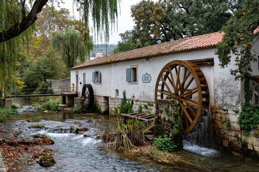 A historic watermill with large wooden wheels, a stone bridge, and a flowing river. 4