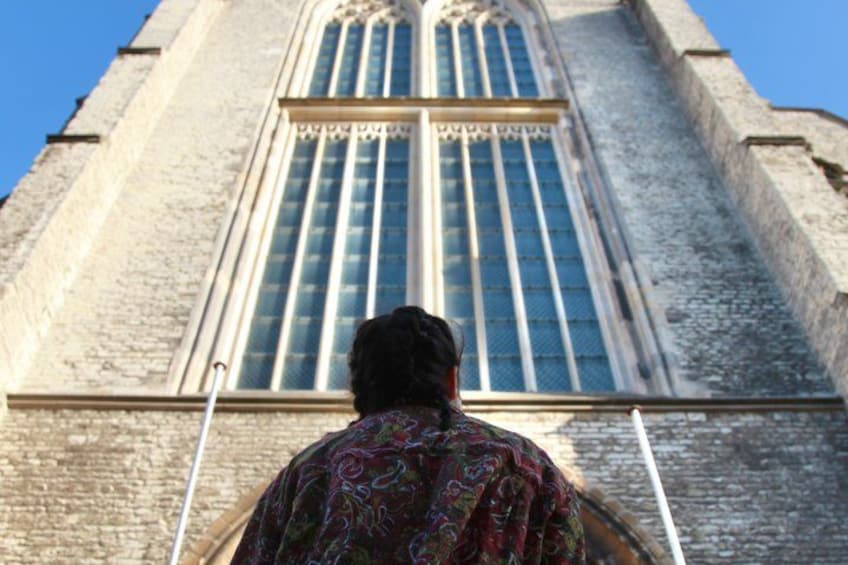 A person standing in front of a tall, historic building with large windows and a stone facade. 3