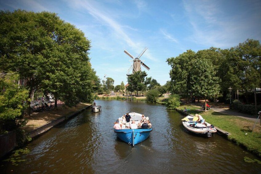 A river with boats, a windmill, and trees. 1