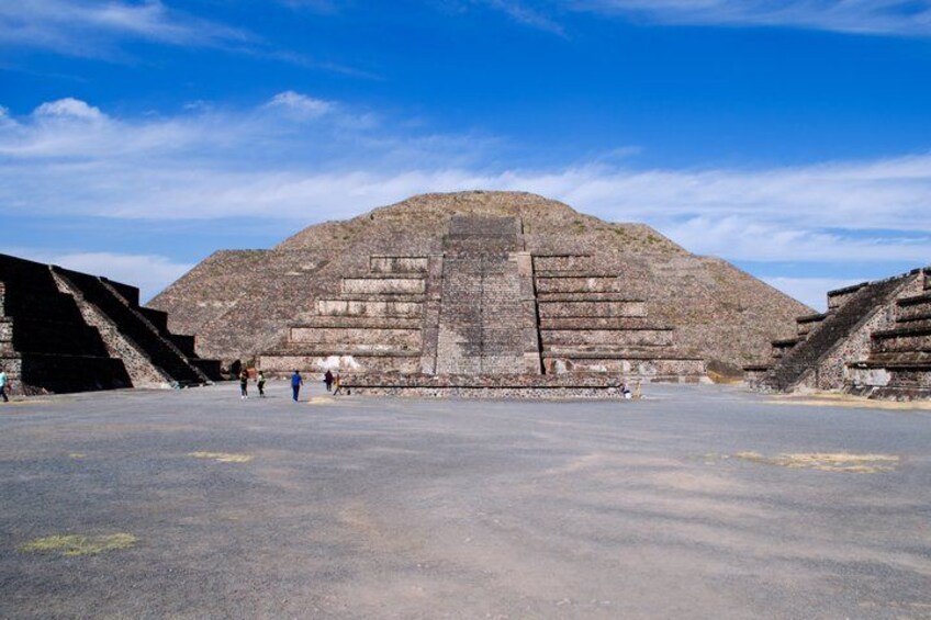 A large pyramid with a flat top, surrounded by a paved area with people walking around. 1