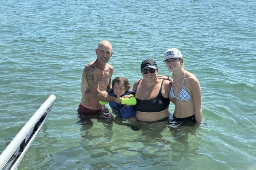 A group of people in a body of water, a boat, and a clear sky. 1