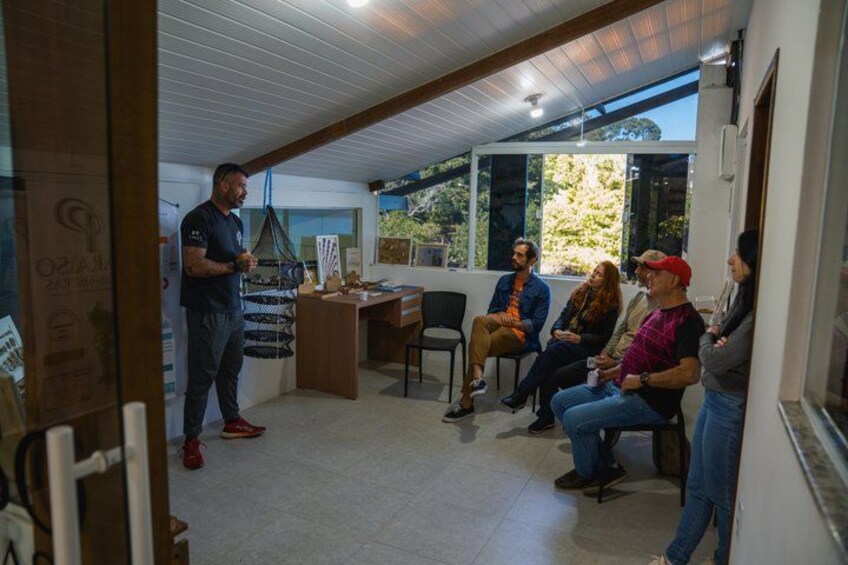 A man standing and talking to a group of seated people in a room with a desk and a window. 5