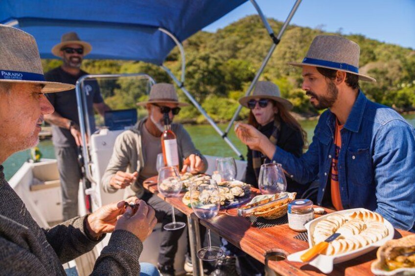 A group of people dining on a boat with a table full of food and drinks. 1