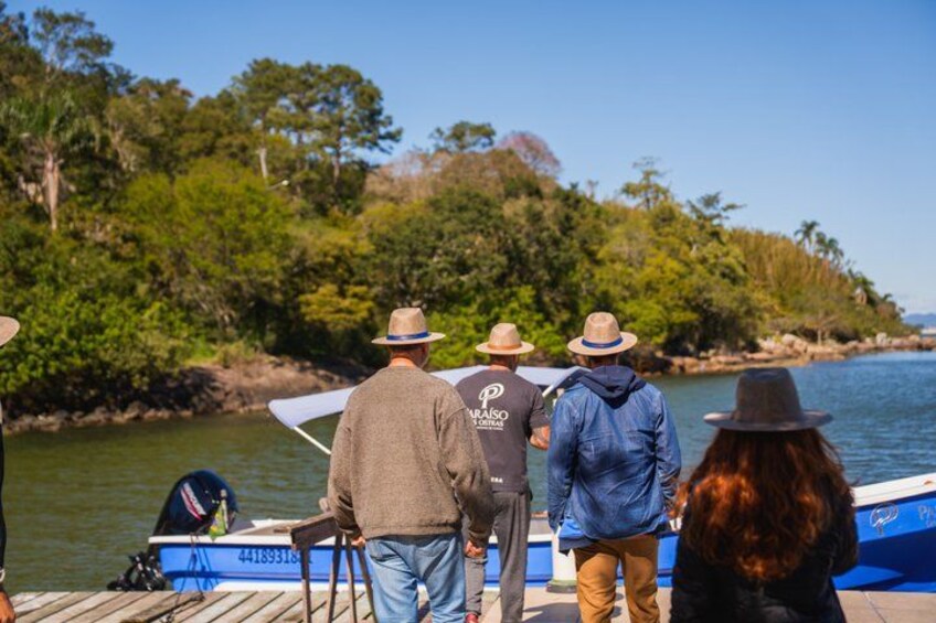 A group of people on a dock by a body of water with a boat and a forested area in the background. 2