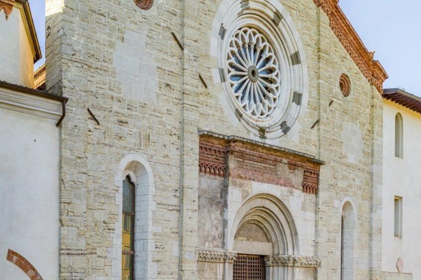 A historic stone building with a large circular window and arched doorways. 5