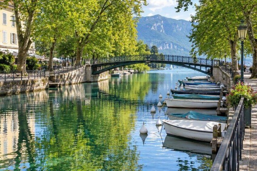A calm river with boats docked, a stone bridge, and a mountainous backdrop. 3