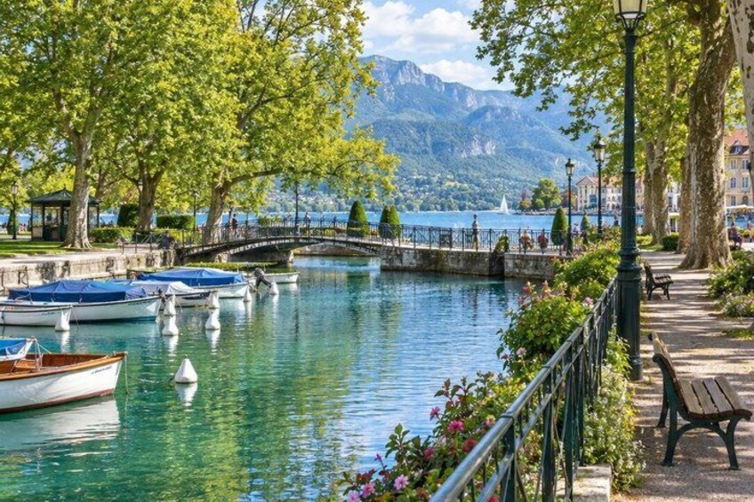 A calm river with boats, a bridge, trees, and a bench along the riverbank. 4