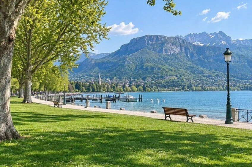 A lakeside park with benches, a lamp post, and a mountain backdrop. 2