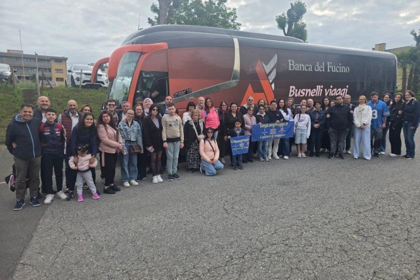 A group of people standing in front of a red bus with the text 'Banca del Fucino Busnelli viaggi' on it. 1