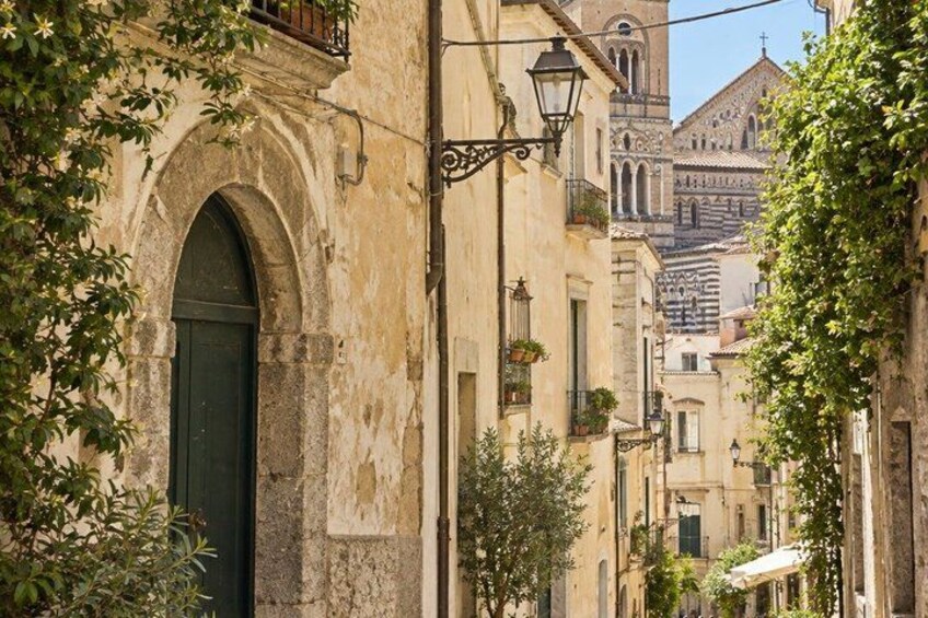A narrow street with old buildings, a green door, and a church in the background. 3