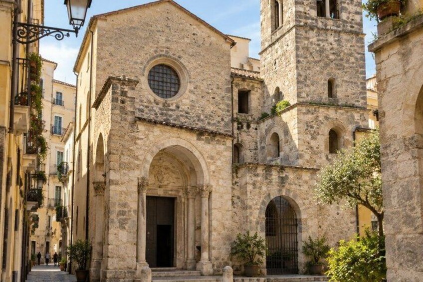 A historic stone building with a bell tower, arched doorways, and a circular window. 5