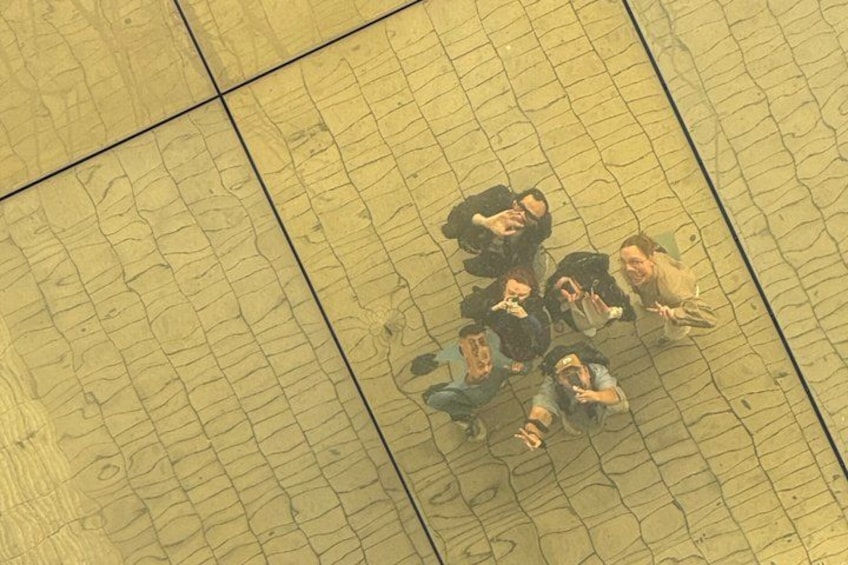A group of people sitting on a tiled floor, possibly in a public space. 5