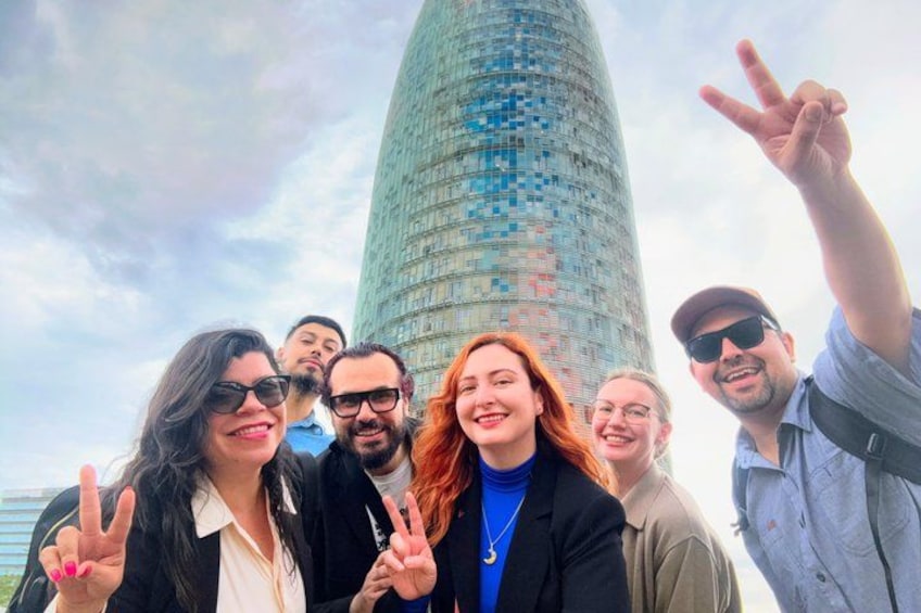 A group of people posing in front of a tall, cylindrical skyscraper with a glass facade. 1