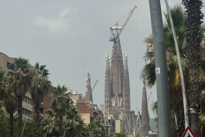 A cityscape with a prominent building featuring a spire and construction cranes, palm trees, and a traffic sign. 3