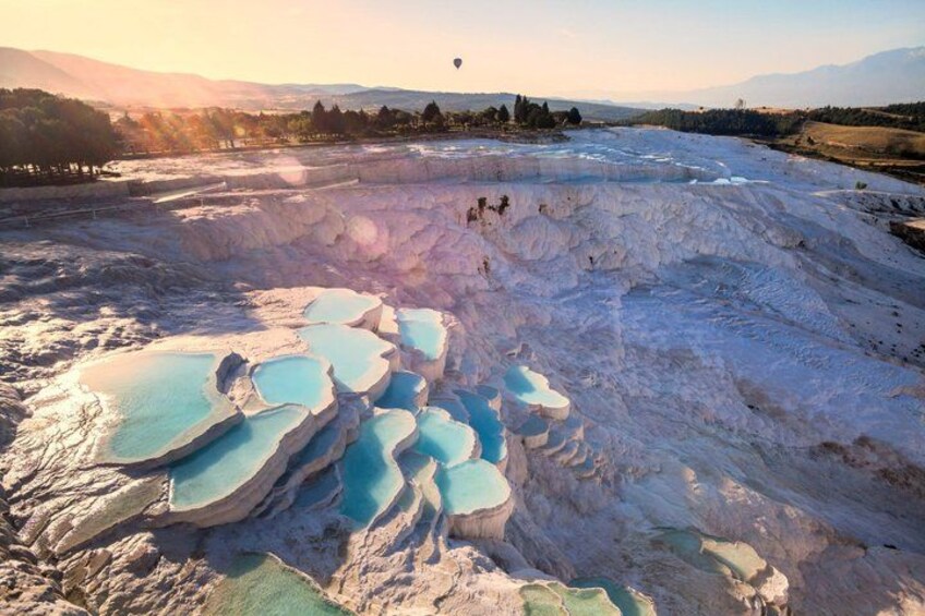 A landscape with terraced pools of mineral water, a clear sky, and distant mountains. 1