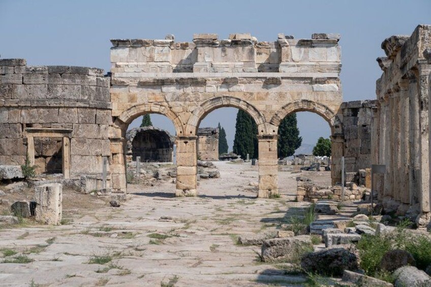 Ancient ruins with stone arches and columns, a pathway, and scattered vegetation. 3