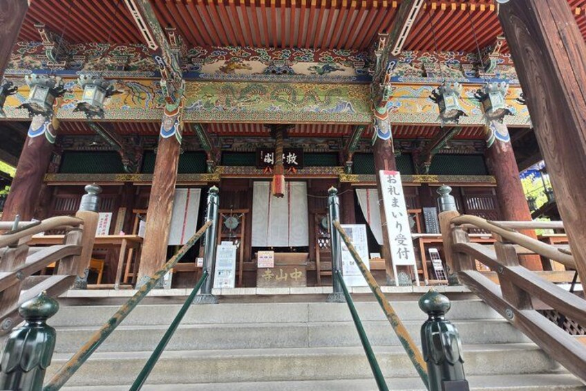A traditional Japanese temple entrance with ornate wooden architecture, a stone staircase, and a signboard. 5