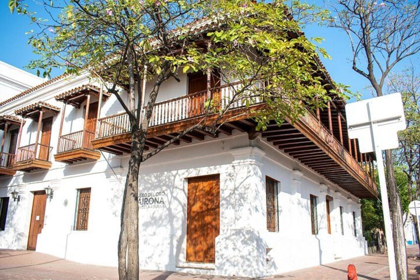 A white building with a wooden balcony, a tree in front, and a clear blue sky. 3