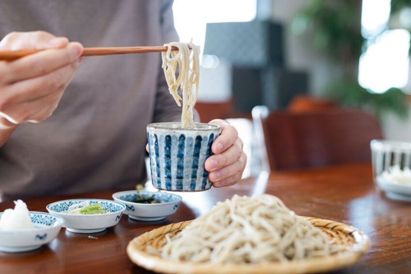 A person eating noodles with chopsticks from a blue and white bowl. 4