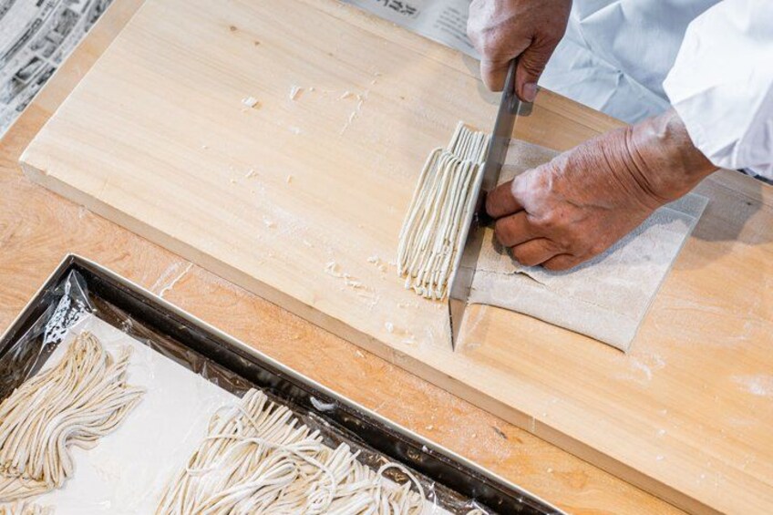 A person cutting noodles on a wooden board. 5