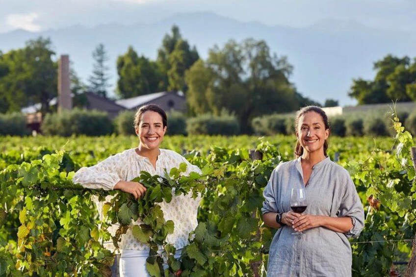 Two people in a vineyard with rows of grapevines and a mountain in the background. 1