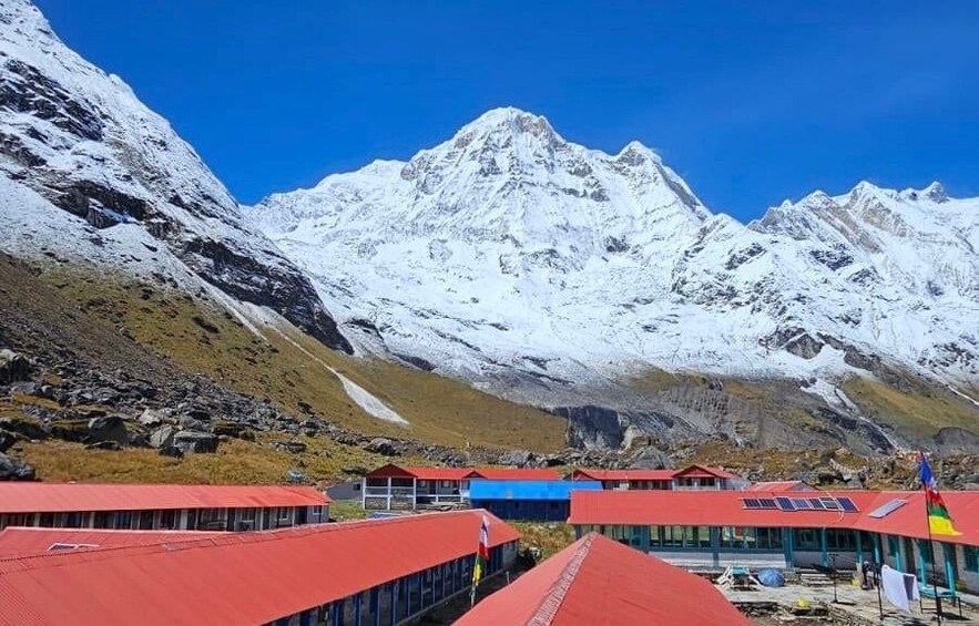 Une chaîne de montagnes enneigées se dresse sous un ciel bleu clair. Au premier plan, on aperçoit des bâtiments aux toits rouges. 4