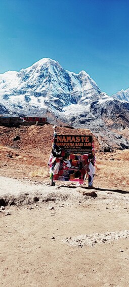Un panneau indiquant « Namaste A.B.C. 4130 mètres » dans un paysage aride et rocheux, avec une montagne enneigée en arrière-plan. 1