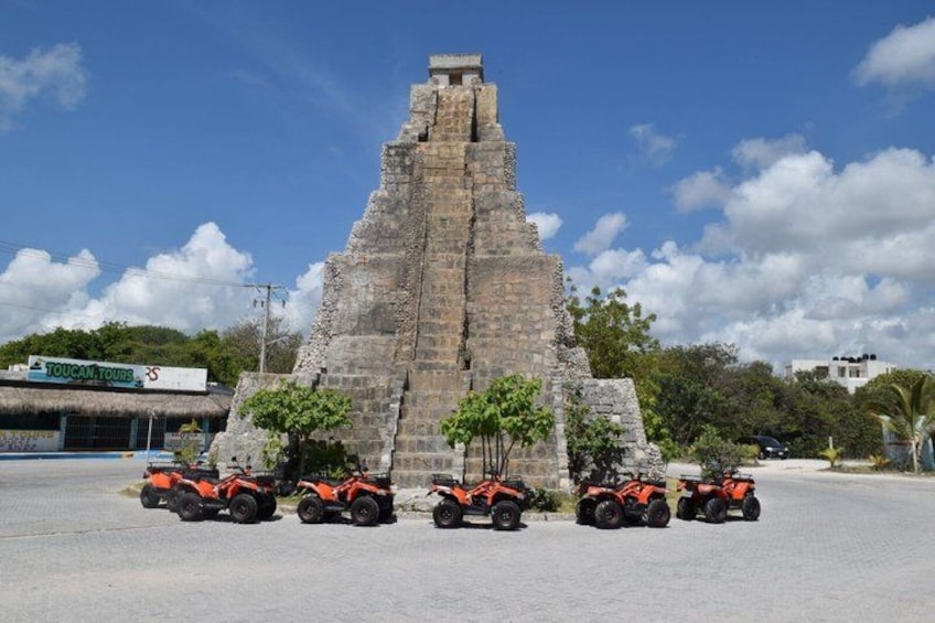 A pyramid structure with four orange off-road vehicles parked in front. 1
