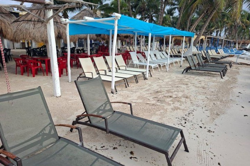 Beach chairs, umbrellas, and tables under a thatched roof. 2
