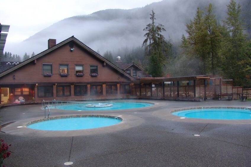 A wooden lodge with two outdoor swimming pools, surrounded by trees and mountains. 5