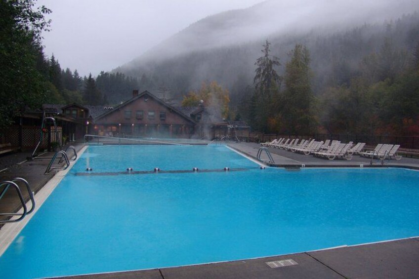 A swimming pool with lounge chairs, a wooden building, and a forested mountain backdrop. 4