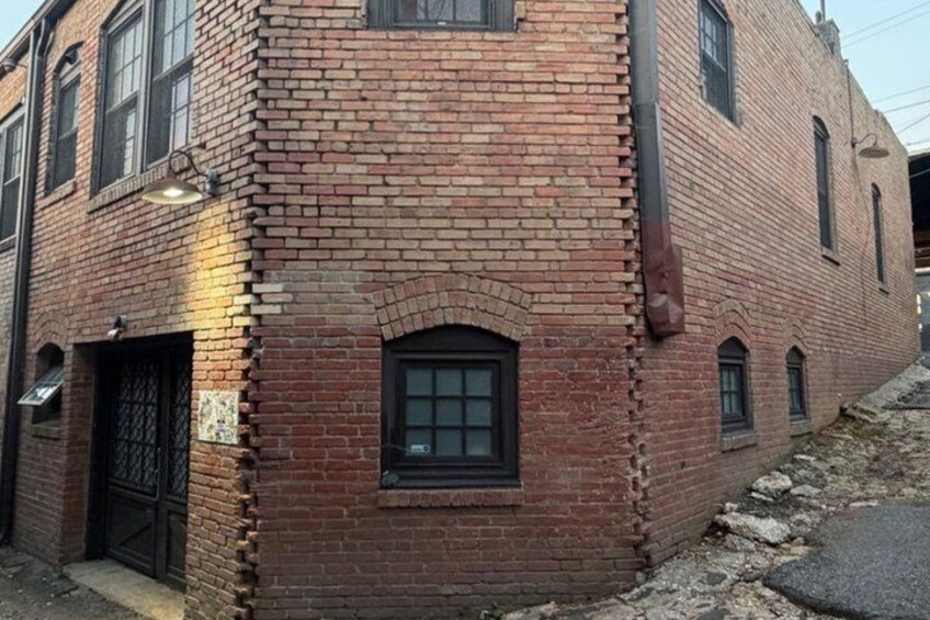 A red brick building with a black window and door, a small arched window, and a brick wall. 5