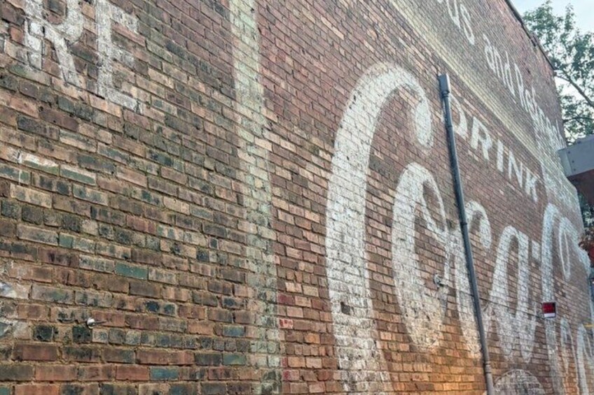 A brick wall with faded graffiti, including the words 'Coca-Cola' and 'Drink'. 3