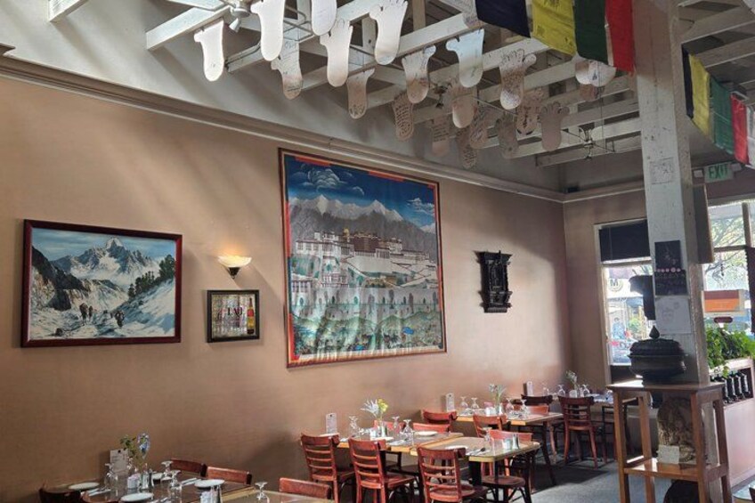 A restaurant interior with tables, chairs, wall art, and a ceiling light fixture. 5